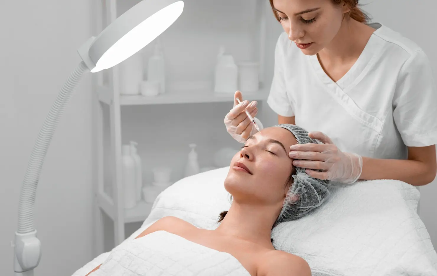 Provider carefully administering a dermal filler injection to a female patient's cheek at a Newton, Acton and Natick med spa